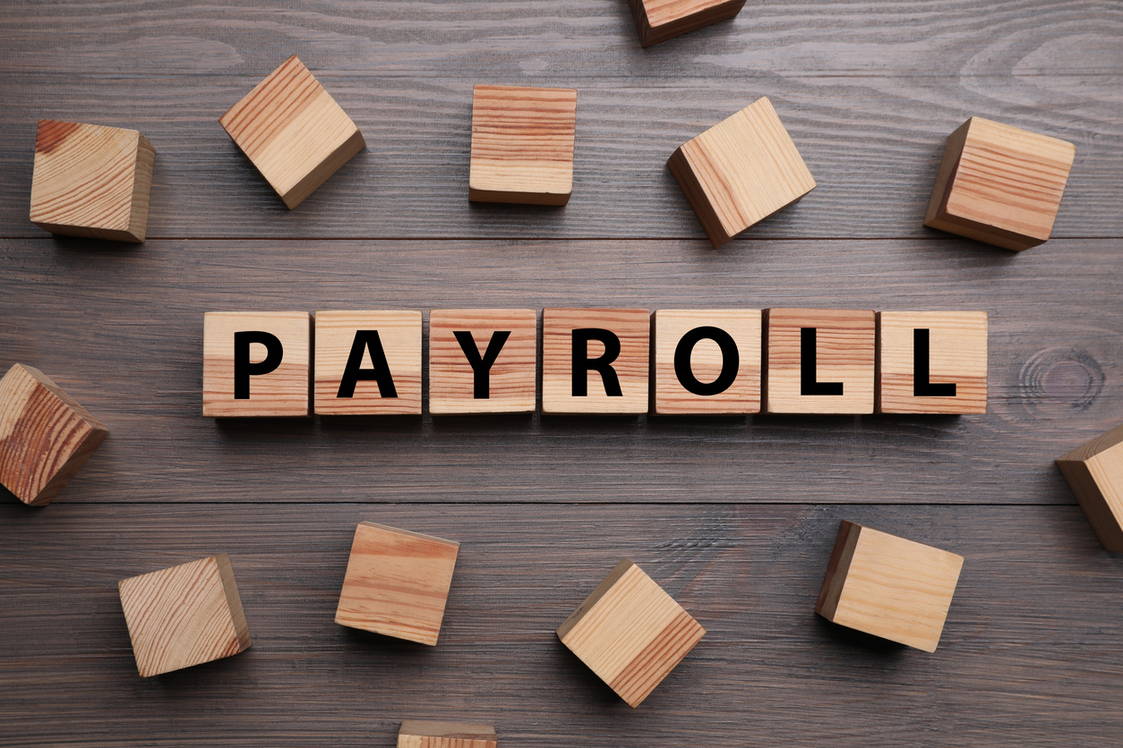 Wooden letter blocks spelling PAYROLL representing high earners living paycheck to paycheck